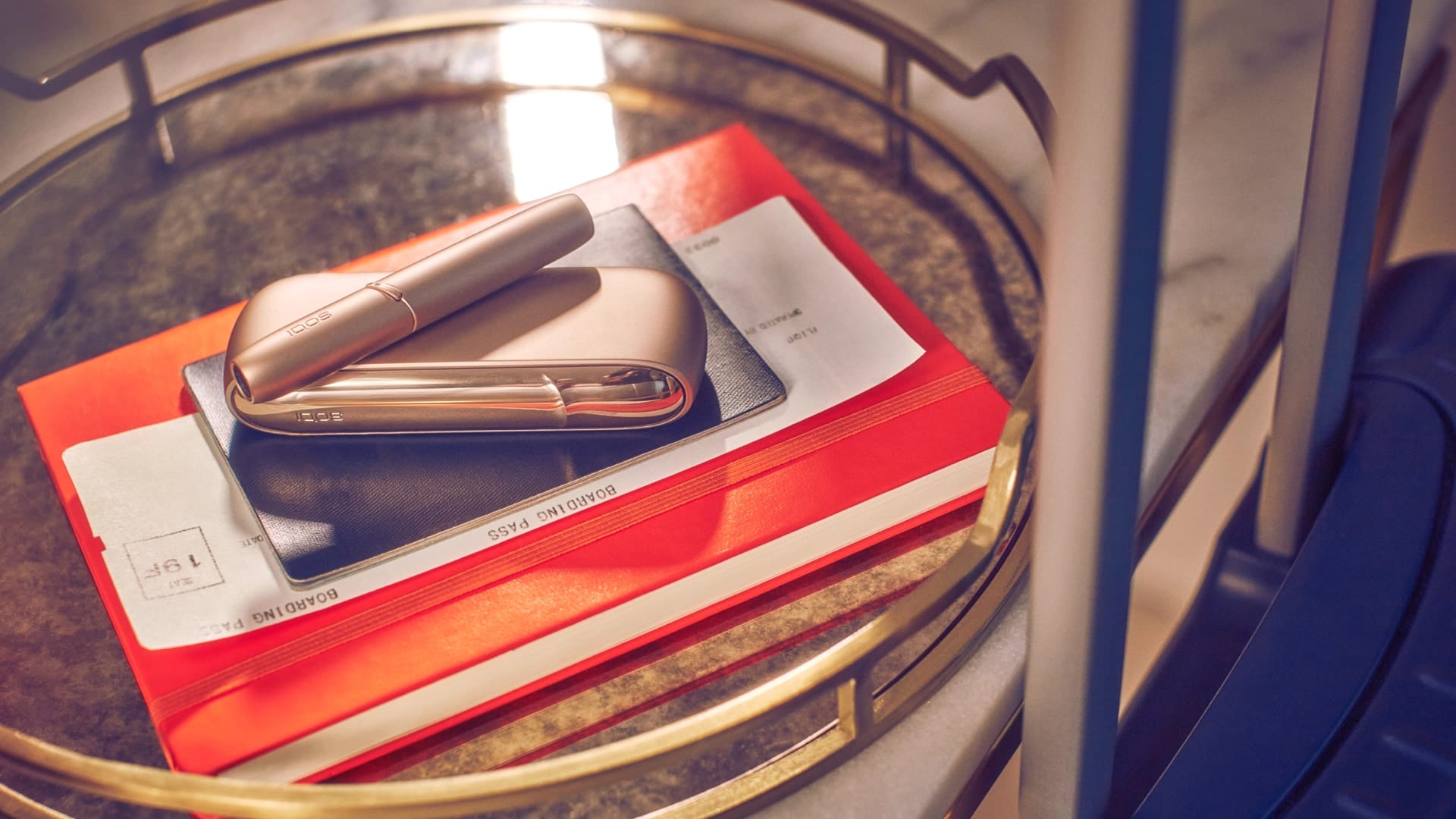 Un dispositivo IQOS DUO dorado sobre una libreta naranja