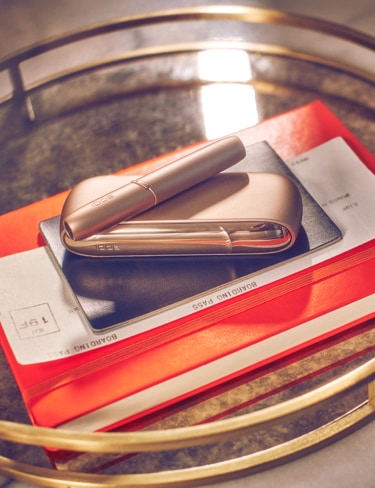 Un dispositivo IQOS DUO dorado sobre una libreta naranja