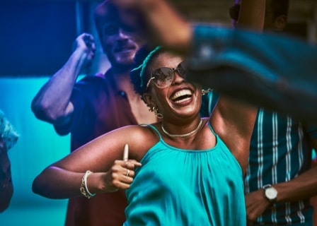 Mujer bailando y sonriendo con un soporte IQOS 3 DUO azul estelar en la mano