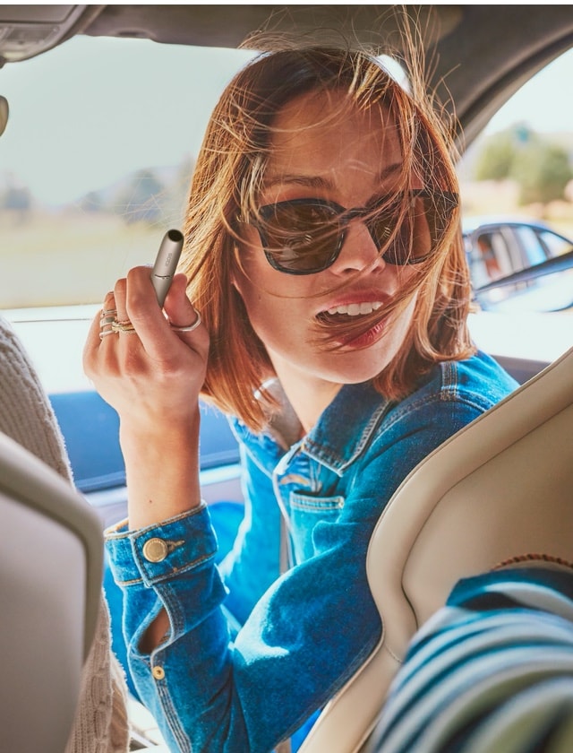 Mujer en un auto con dispositivo IQOS en la mano