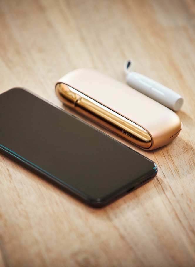 Un celular y un kit IQOS dorado sobre una mesa