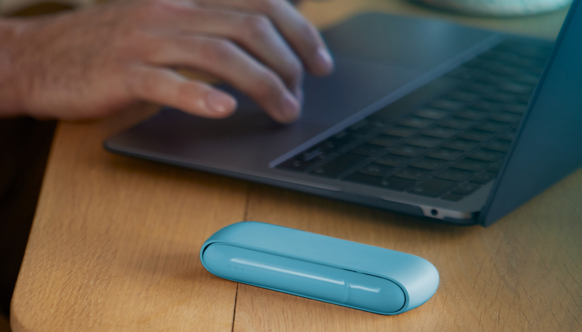 Manos escribiendo en una laptop y Iphone al lado de un Pocket charger de IQOS ORIGINALS DUO