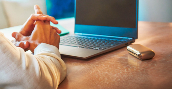 Hombre usando su computadora portátil con su dispositivo IQOS sobre la mesa