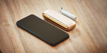 Un celular y un kit IQOS dorado sobre una mesa