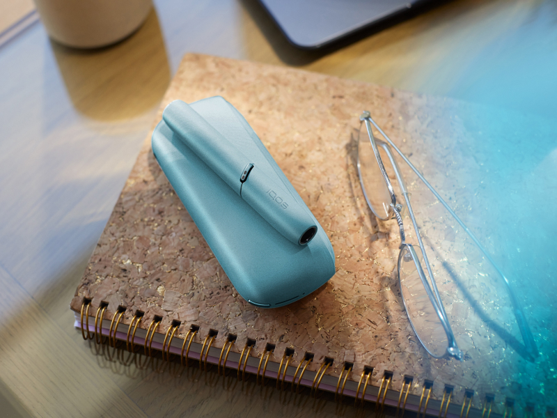 Dispositivo IQOS Originals Duo turquesa sobre una libreta junto a unos lentes