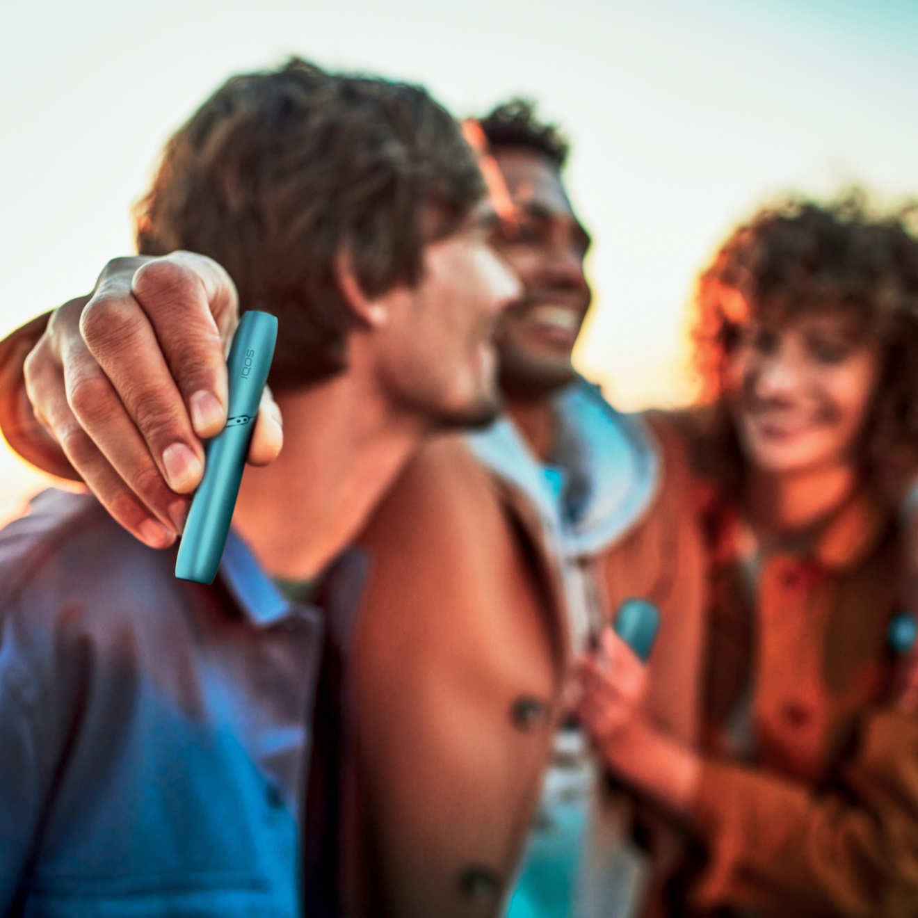 Dispositivo que calienta tabaco IQOS Originals DUO en turquoise, agarrado por personas sonriendo.