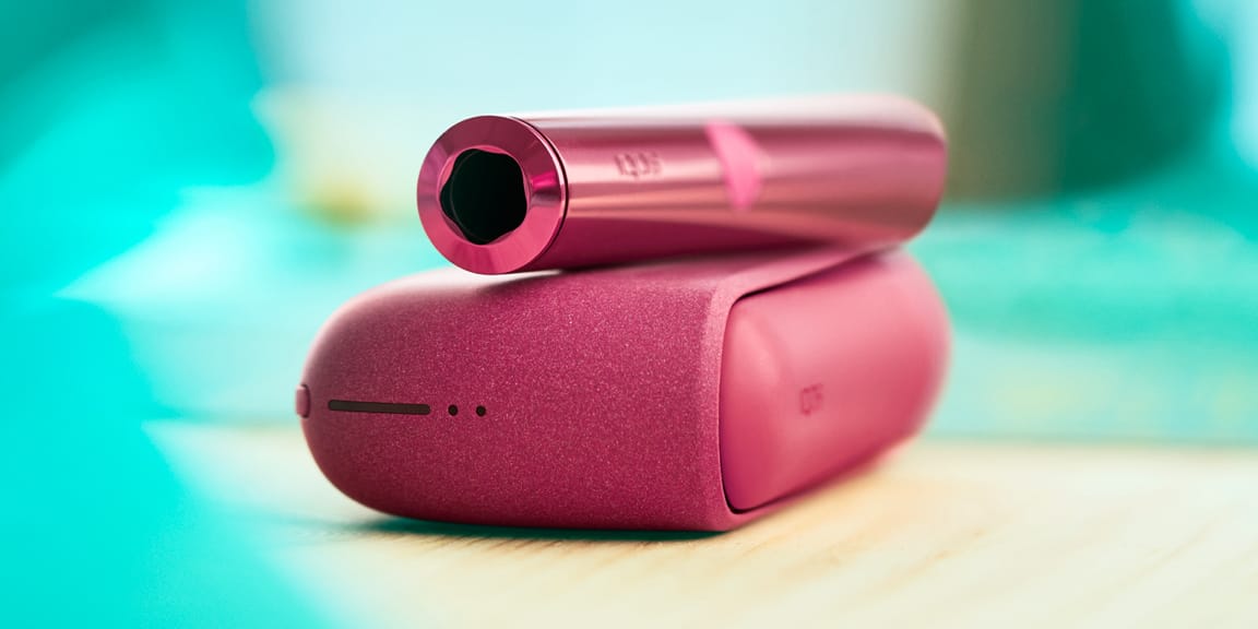 Una mujer sostiene un dispositivo IQOS ILUMA mientras mira hacia una computadora portátil.