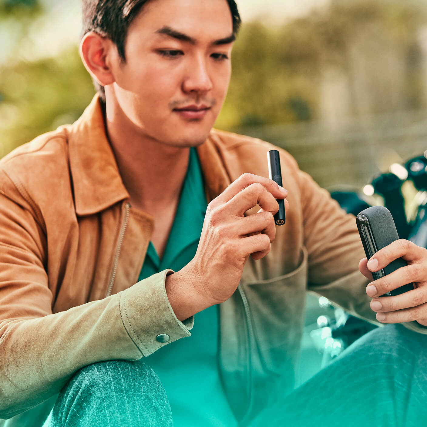 Hombre sosteniendo un IQOS ILUMA PRIME Holder Obsidian Black mientras mira su teléfono móvil.