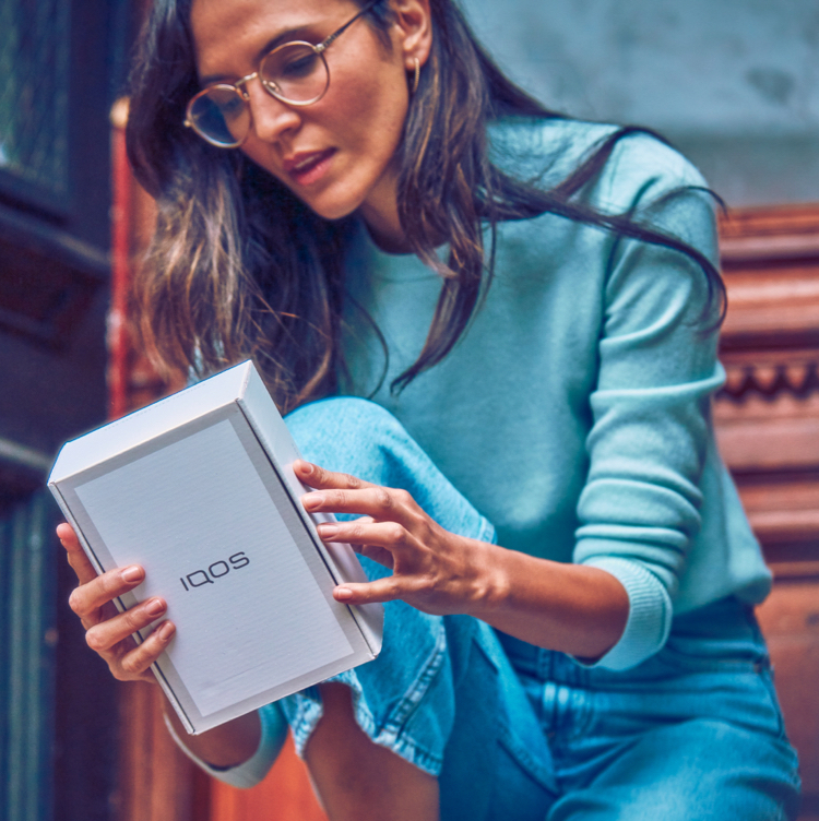 Mujer mirando la parte trasera de un estuche de IQOS.