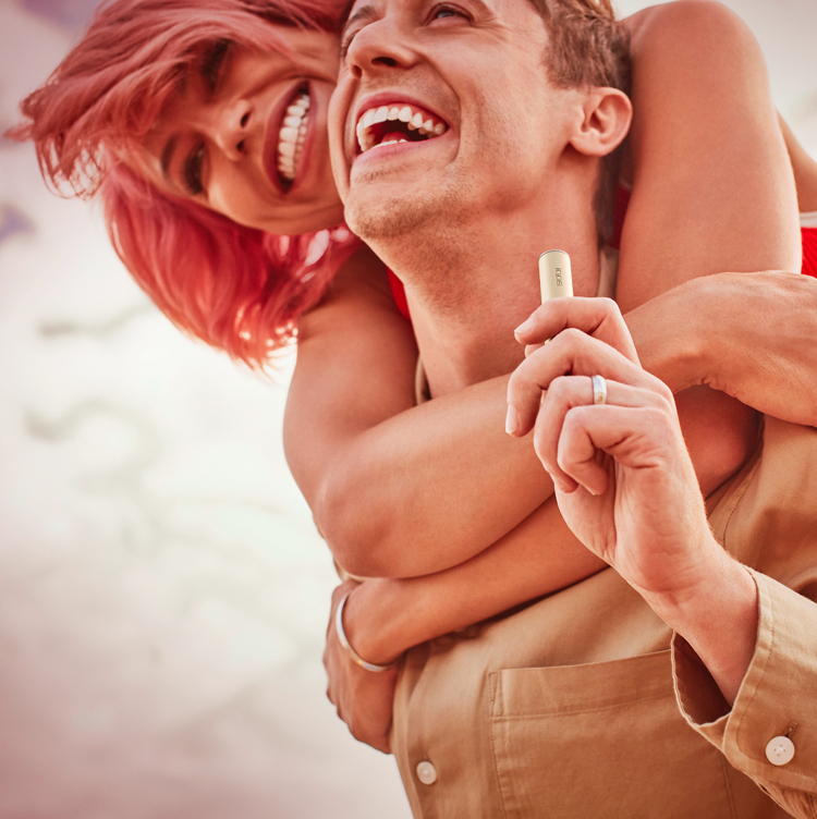 Hombre sosteniendo un dispositivo IQOS mientras lo abraza un compañero.