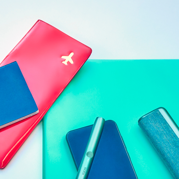 Documentos de viaje, un teléfono celular, un IQOS ILUMA PRIME Holder y Pocket Charger en una mesa.