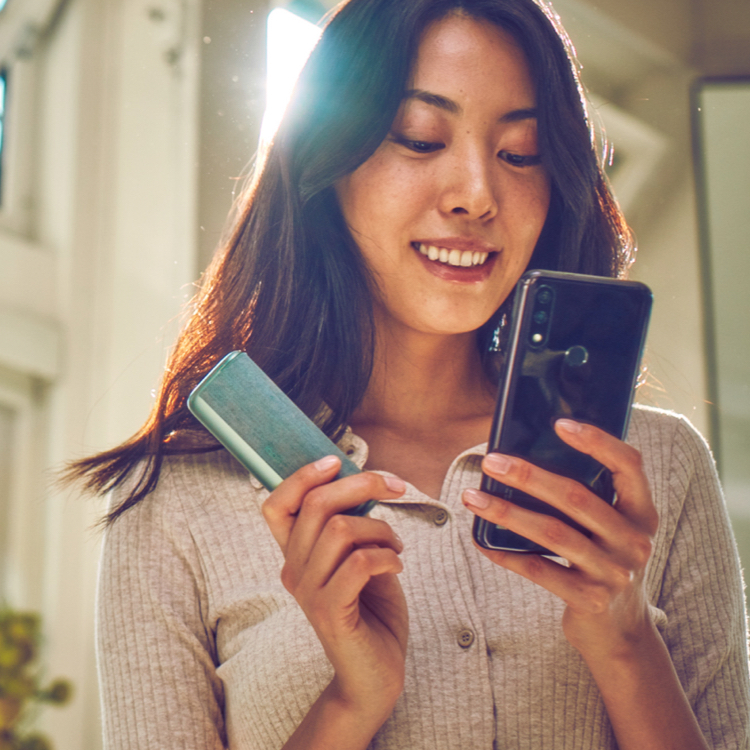 Una mujer usa un celular y sostiene un dispositivo IQOS Iluma