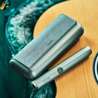 A Jade Green IQOS ILUMA PRIME Holder and Pocket Charger on a guitar.