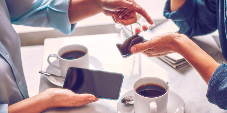 Dos personas sosteniendo sus teléfonos sobre dos tazas de café.