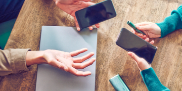 Unas manos sostienen teléfonos celulares y un dispositivo IQOS