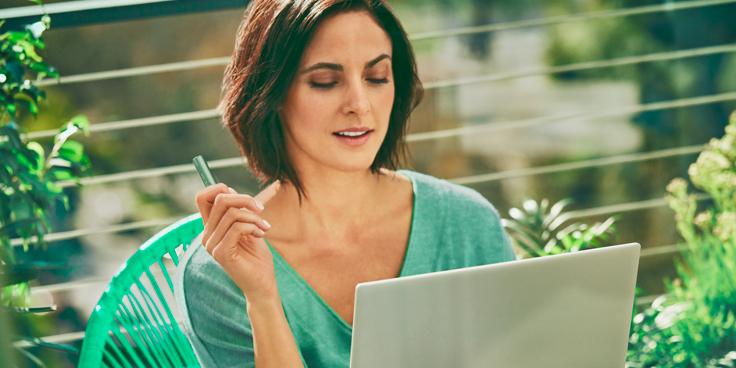 Mujer sosteniendo un dispositivo IQOS mientras mira hacia una computadora portátil.