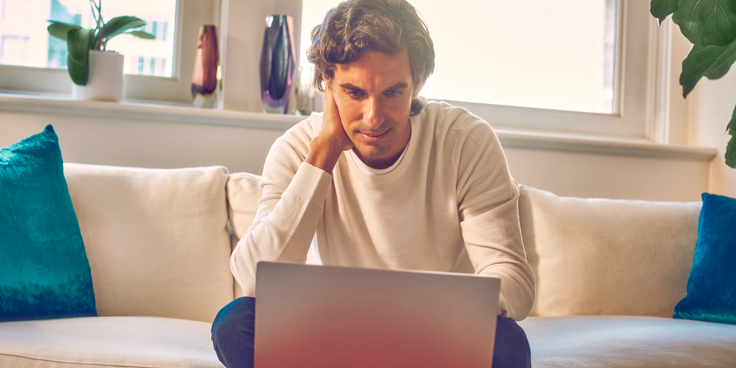Un hombre sentado en un sofá mirando hacia una computadora portátil.