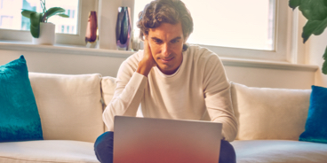 Hombre sentado en un sofá mirando una computadora portátil.